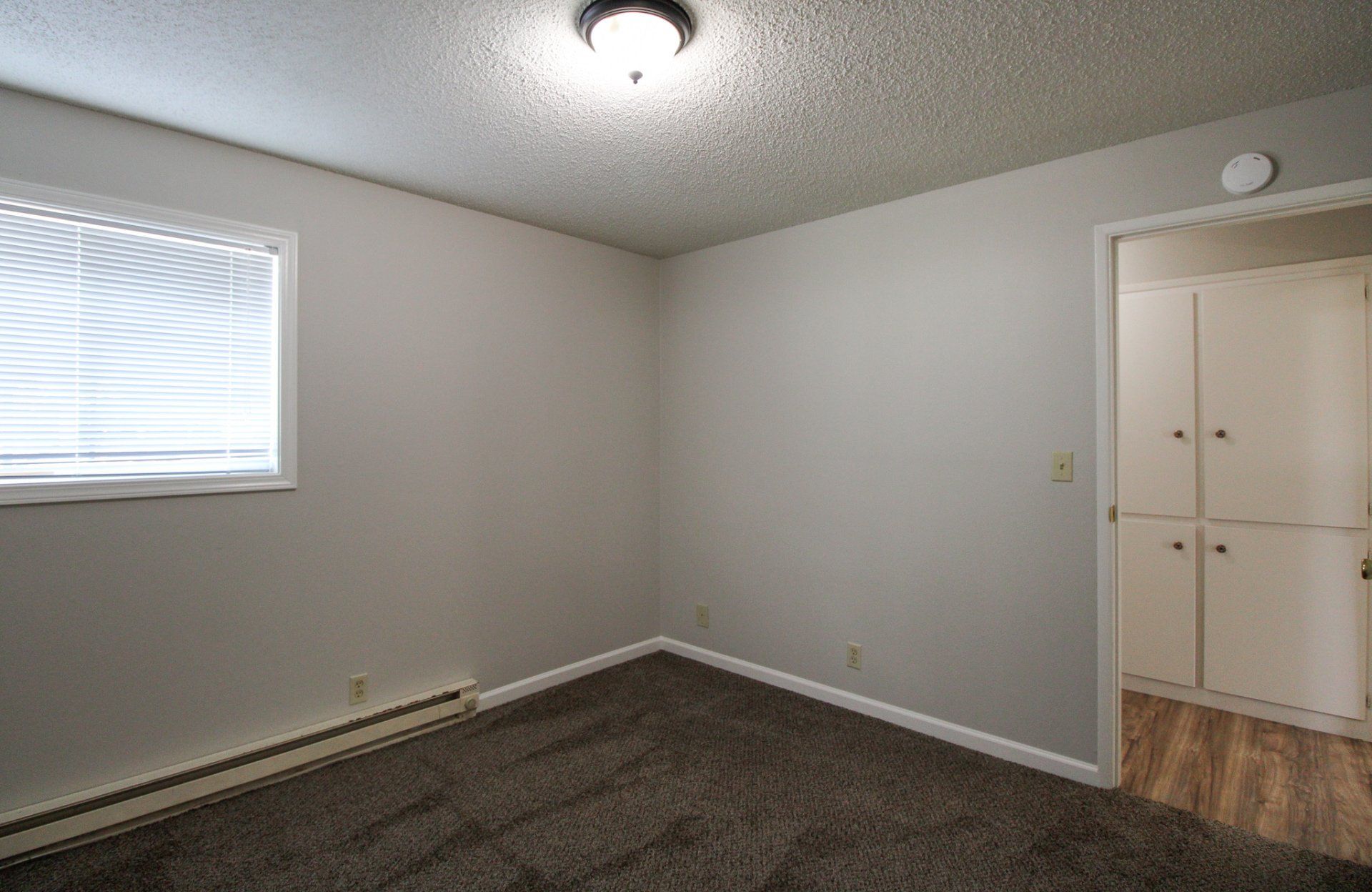 An empty bedroom with a window and a ceiling light.