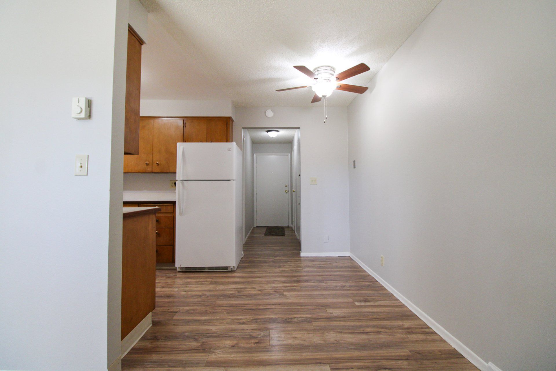 An empty kitchen with a refrigerator and a ceiling fan