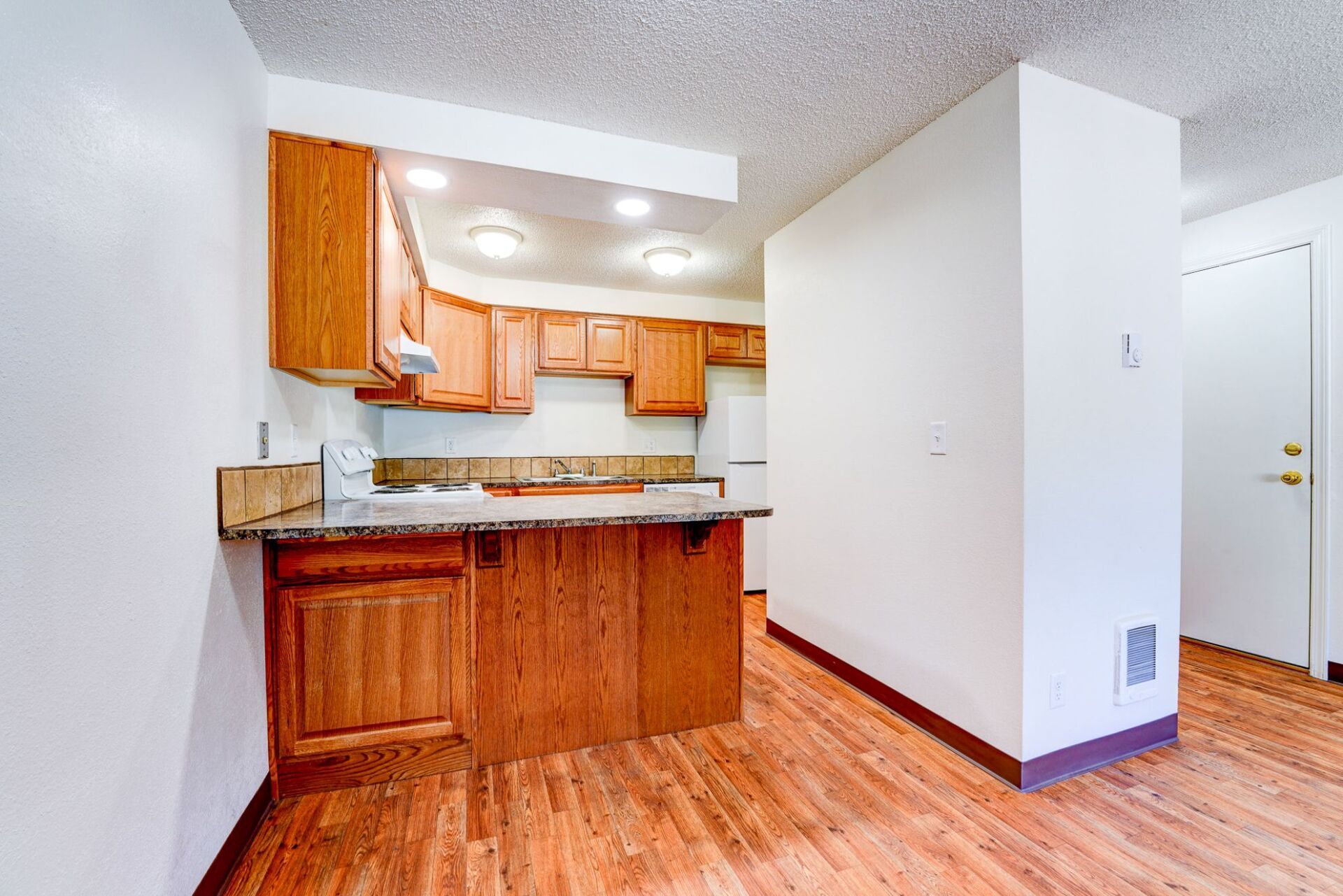 A kitchen with wooden cabinets and hardwood floors in a house.