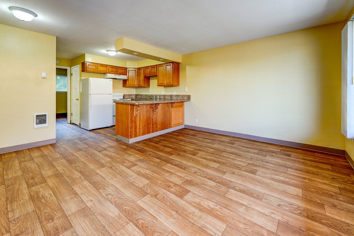 A living room with hardwood floors and a kitchen in the background.