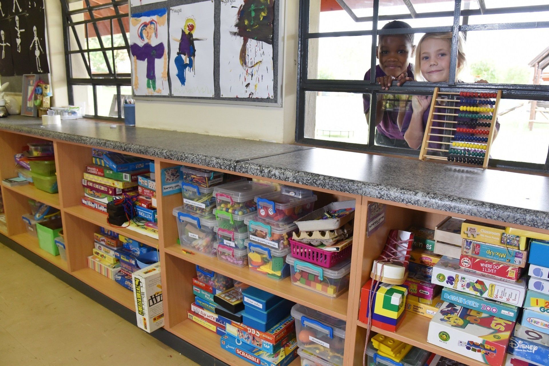 two children are looking out a window at a shelf full of toys .