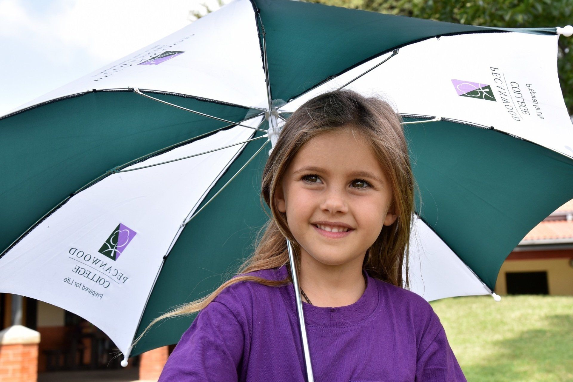 a young girl in a purple shirt is holding a green and white umbrella .