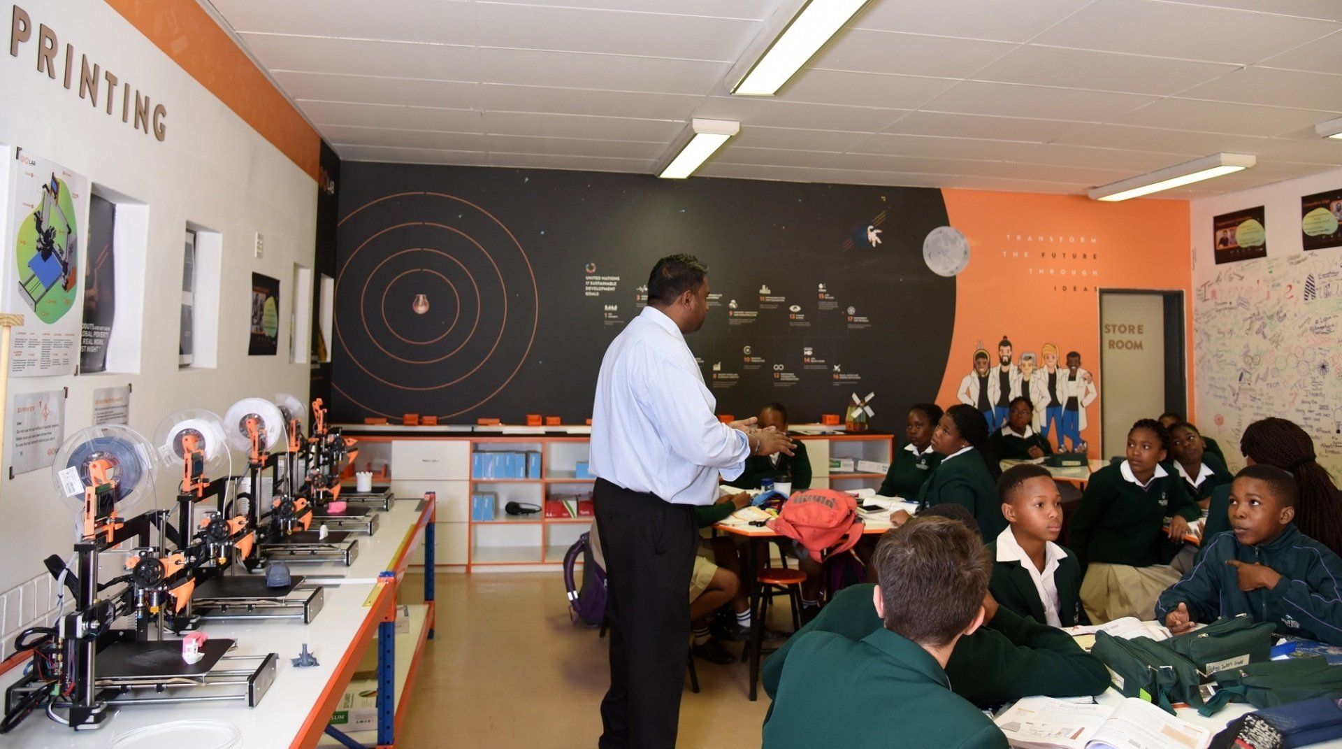 a teacher stands in front of a group of children in a classroom with the word printing on the wall