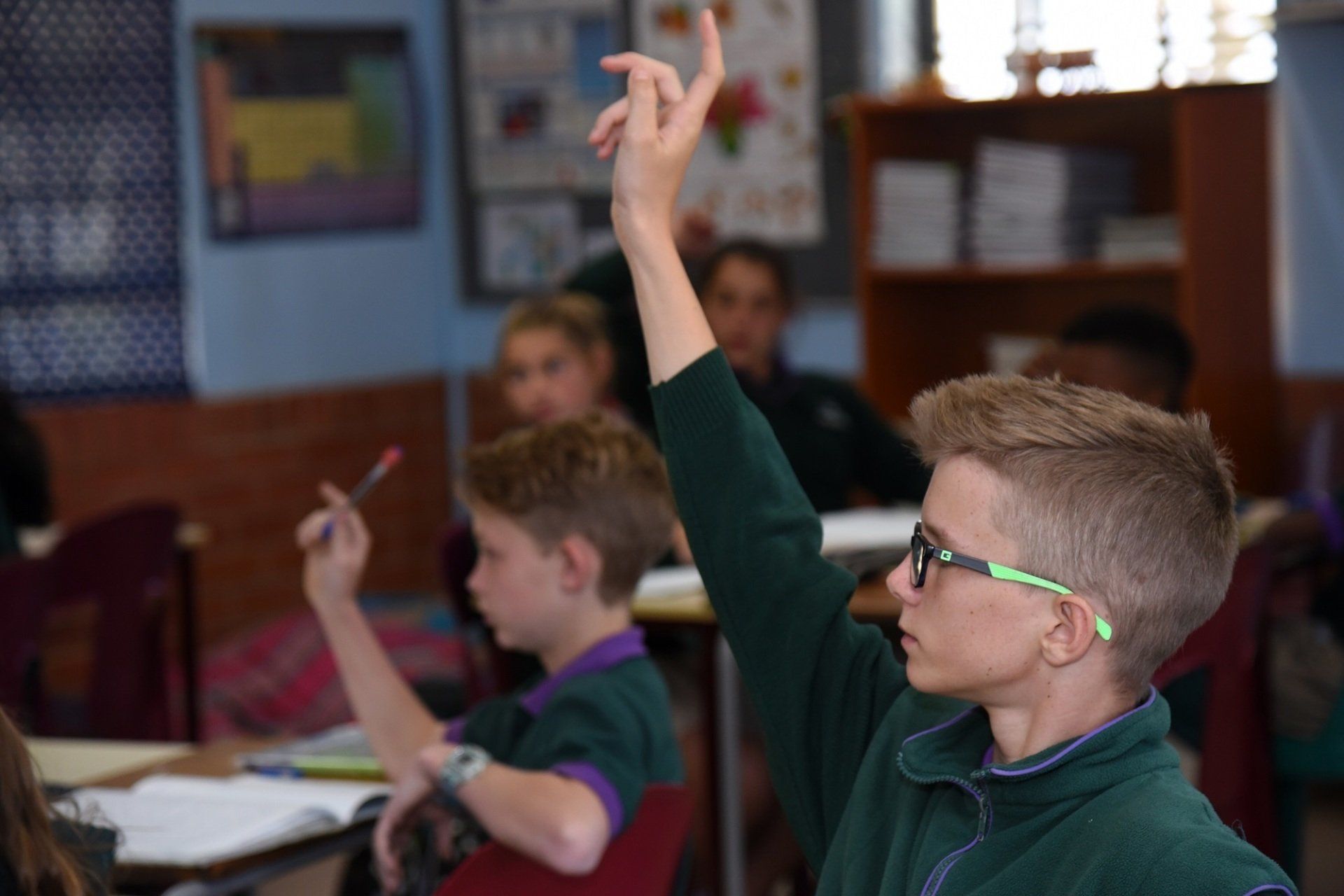 a boy is raising his hand in a classroom to answer a question .