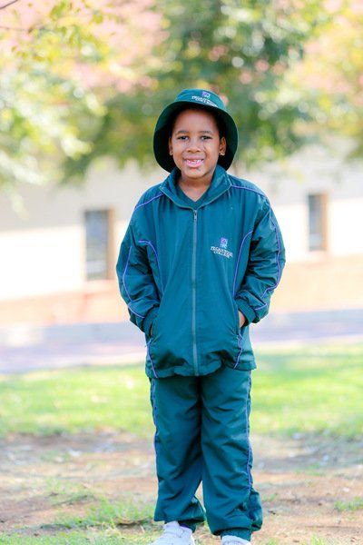 a young boy wearing a green jacket and hat is standing in a park .