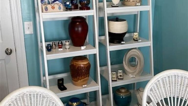 A room with two chairs and two shelves filled with vases and urns.