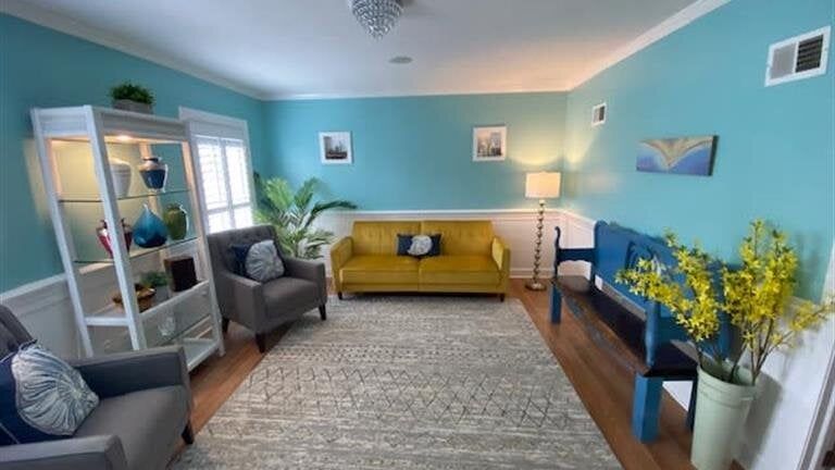 A living room with blue walls , a yellow couch , two chairs , and a bench.
