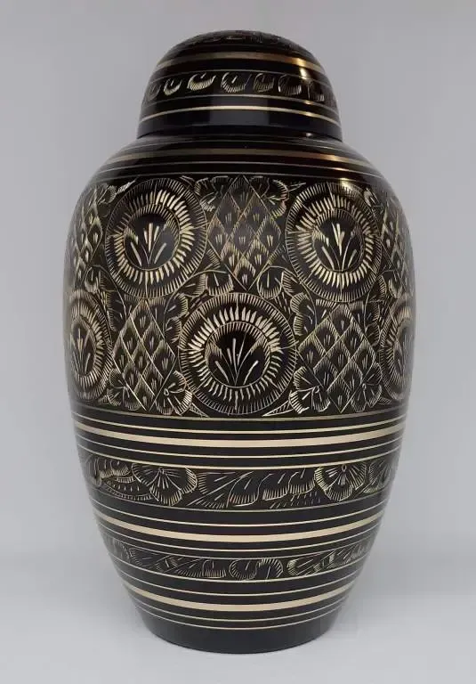 A black vase with a gold pattern on it is sitting on a white table.