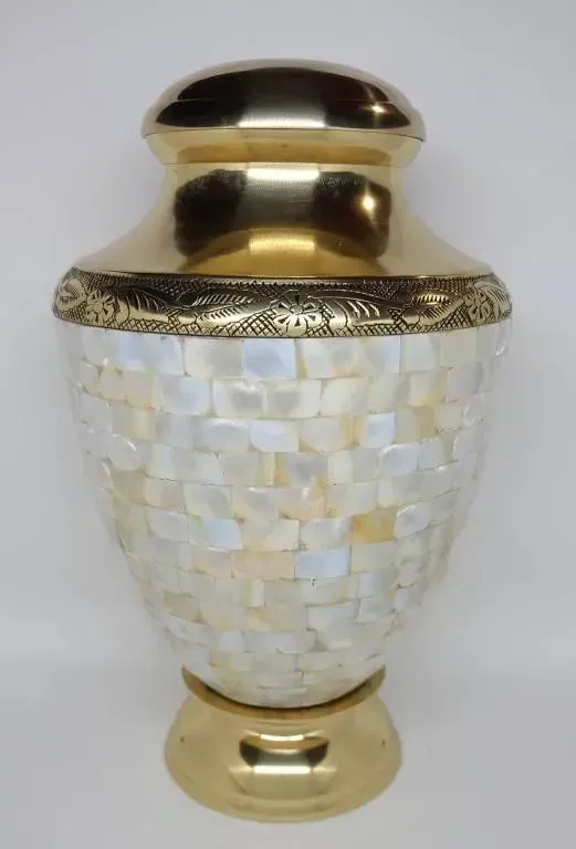 A white vase with a gold lid is sitting on a white surface.