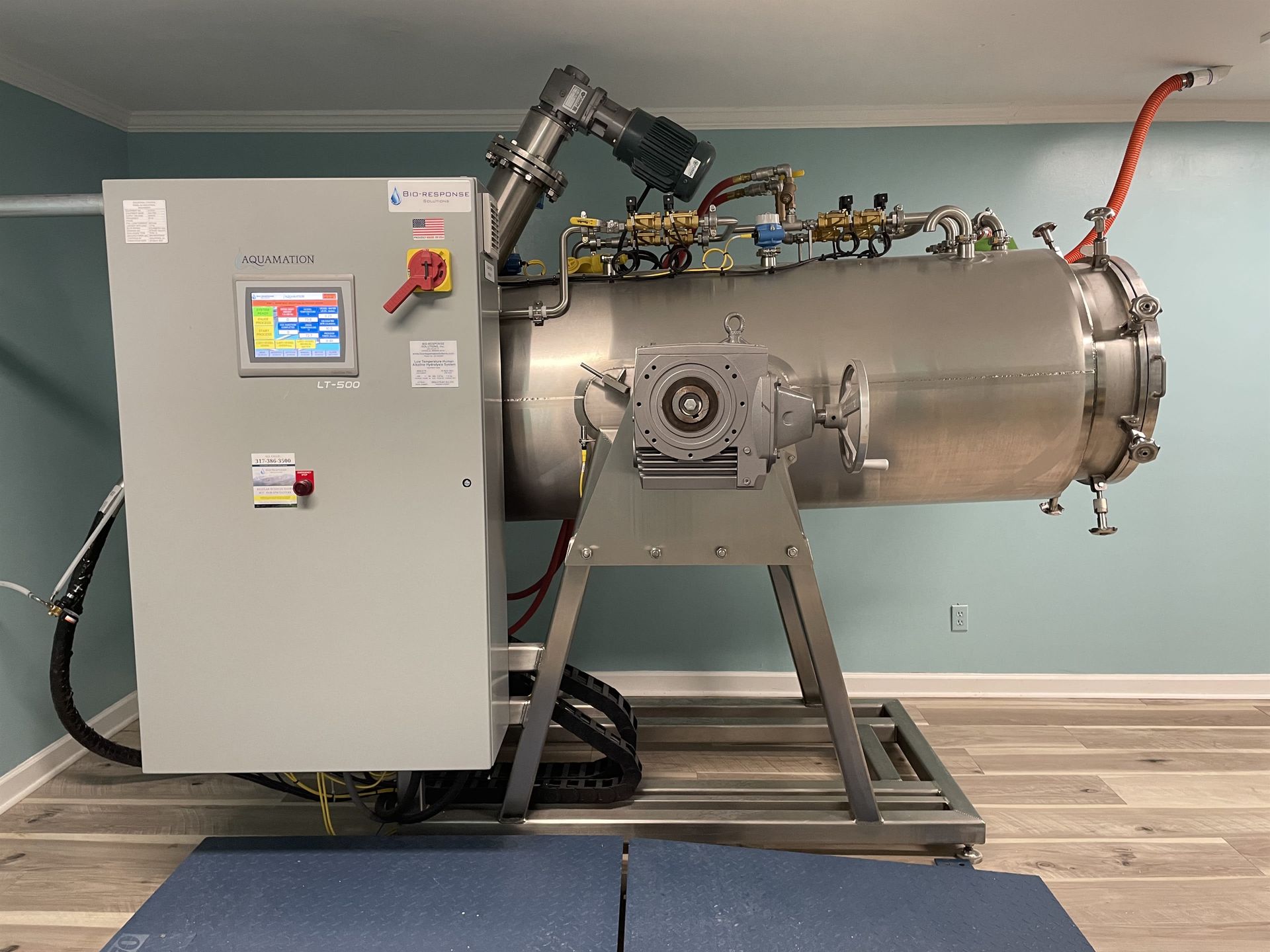 A large stainless steel machine is sitting on a wooden floor in a room.
