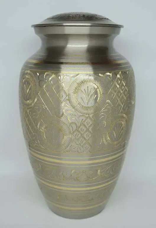 A silver vase with a gold design on it is sitting on a white surface.