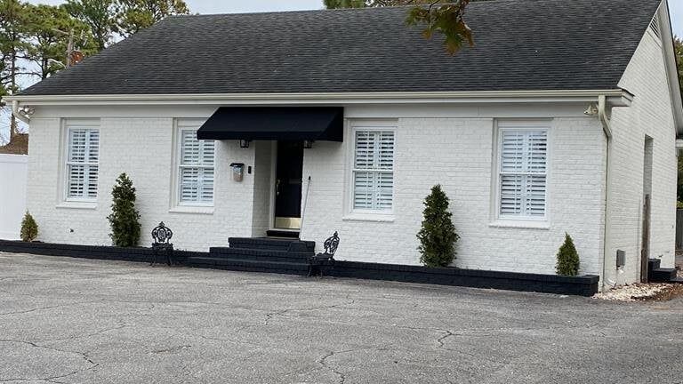 A white brick house with a black roof and a black awning.