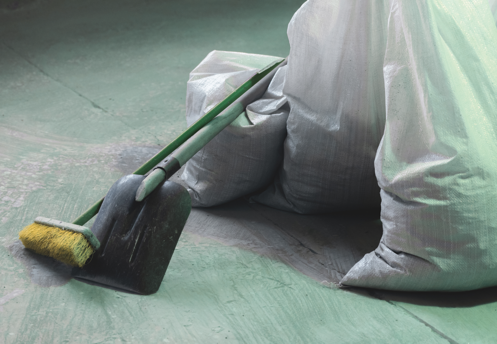 A broom and shovel are sitting on the floor next to a bag.