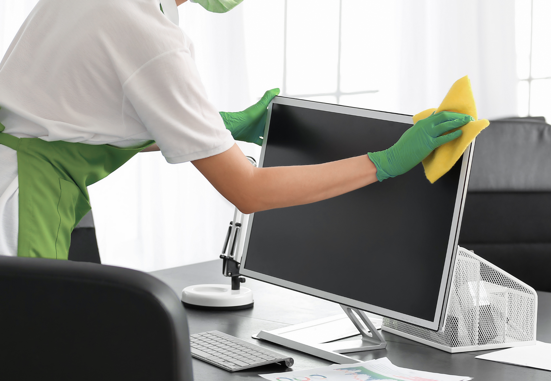 A person wearing yellow gloves is cleaning a desk in front of a computer.