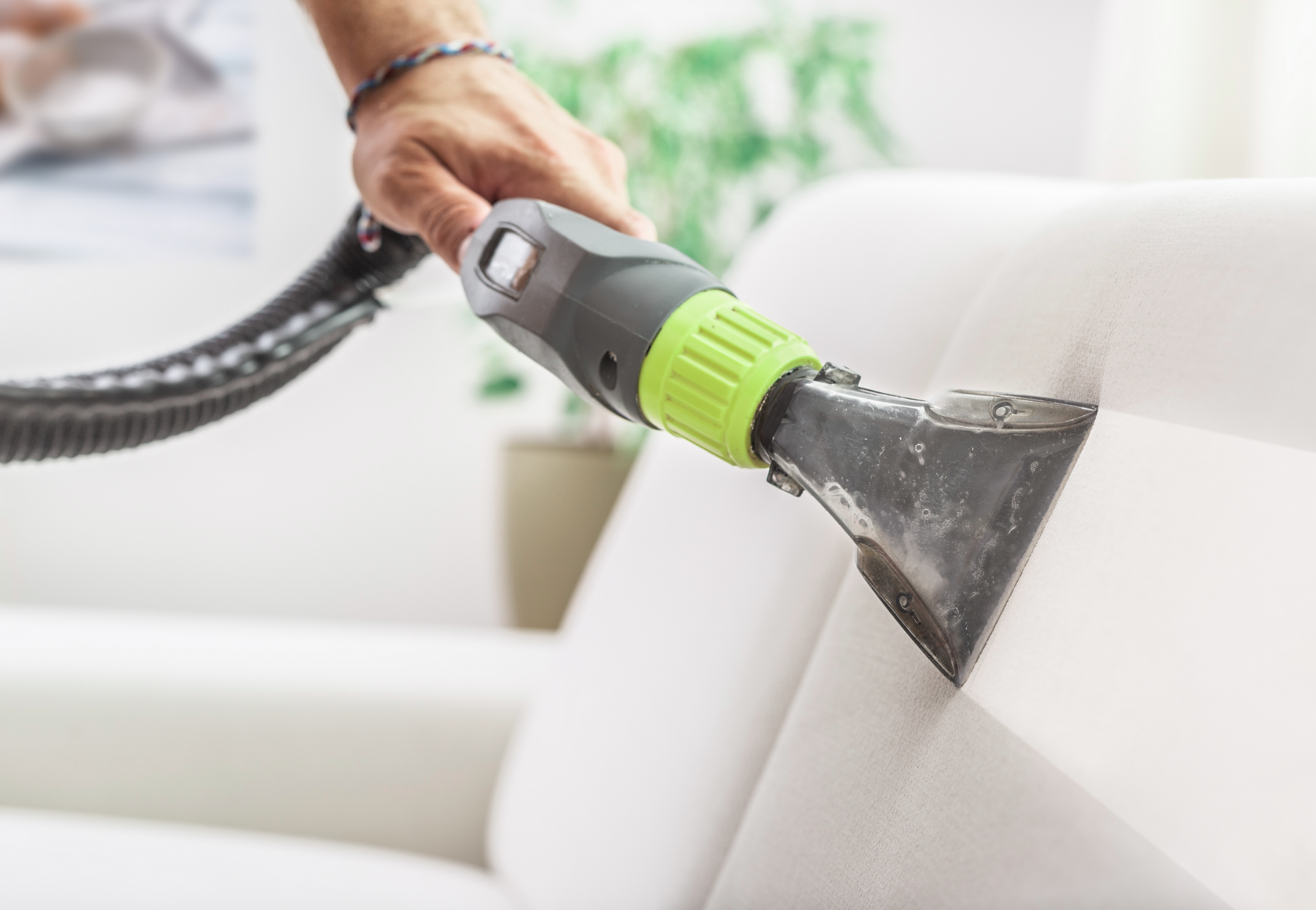 A person is cleaning a couch with a vacuum cleaner.
