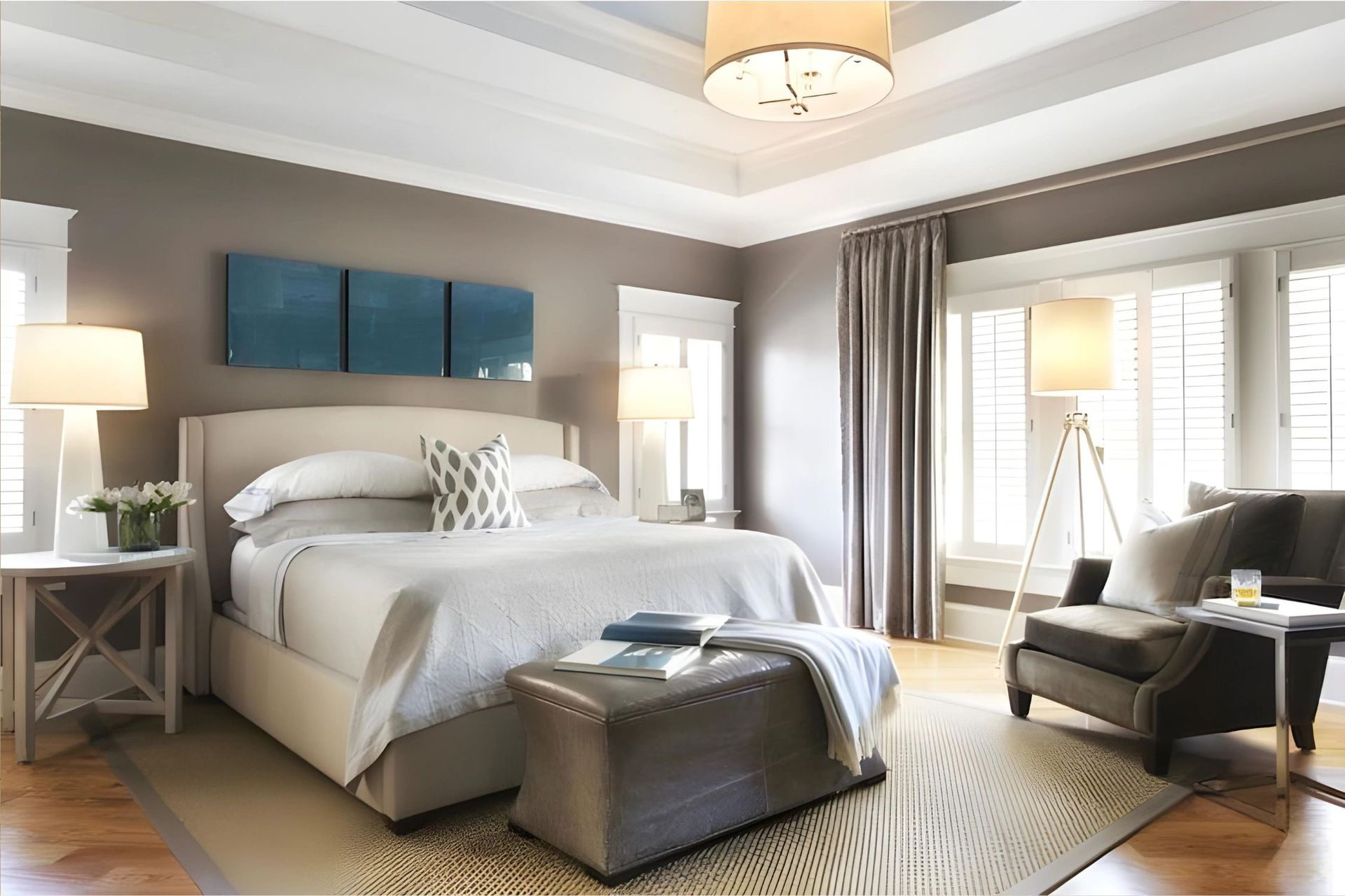 A bedroom with a king size bed , ottoman , chair and lamps.