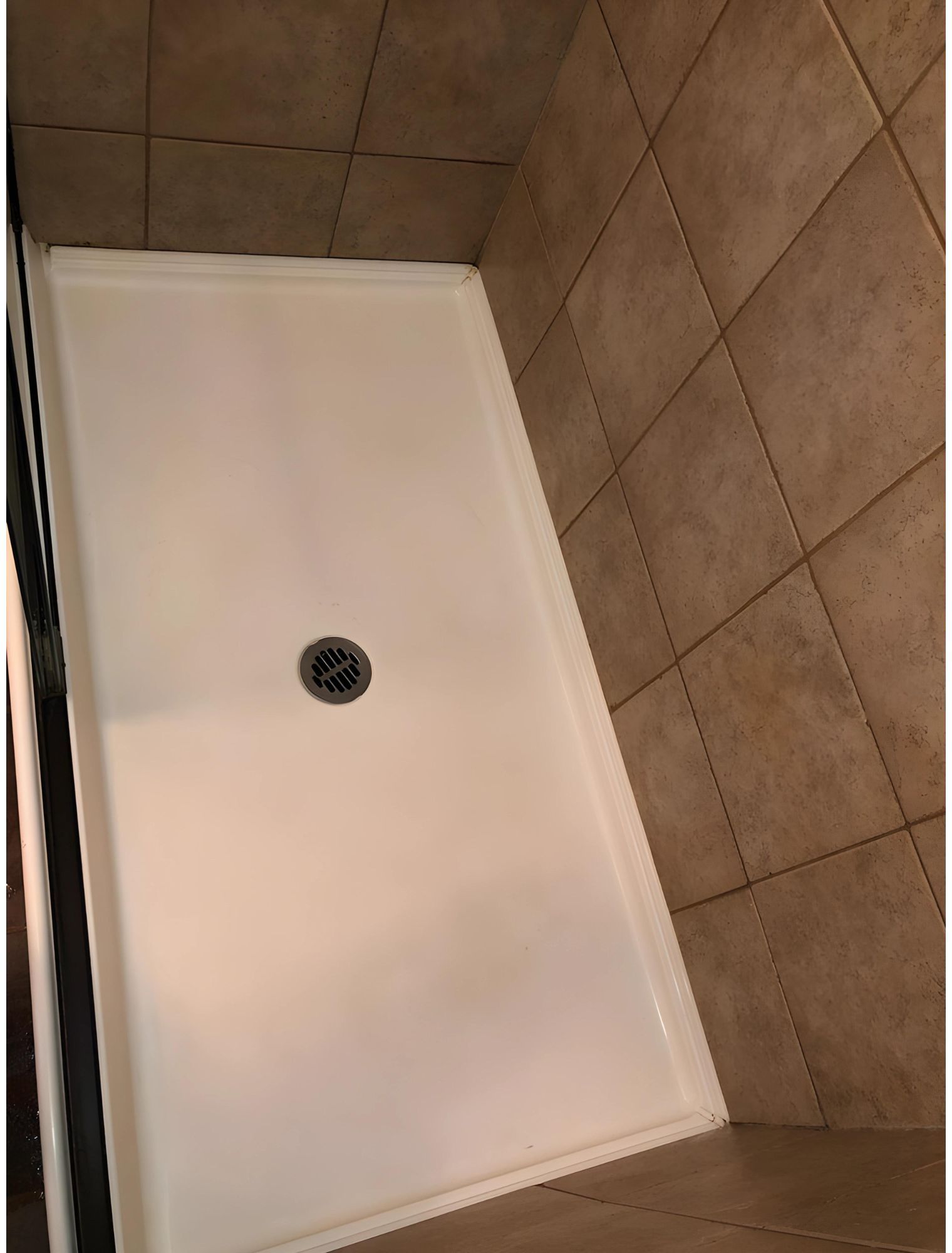 A white shower stall with a drain in a bathroom.