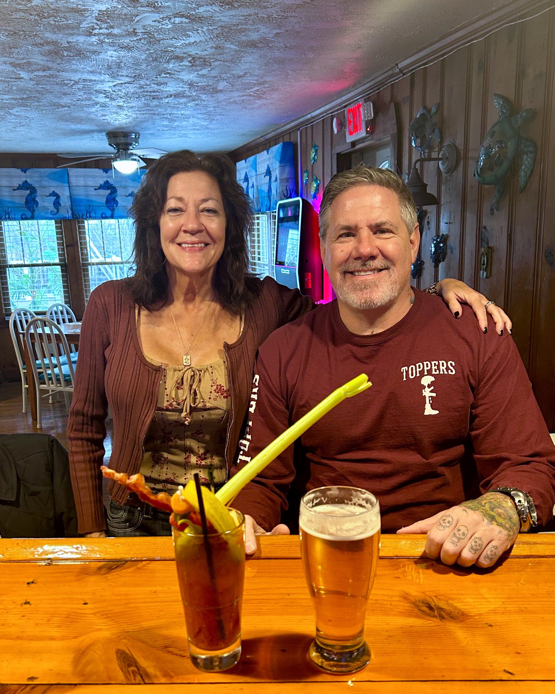A man and a woman are sitting at a bar with drinks.