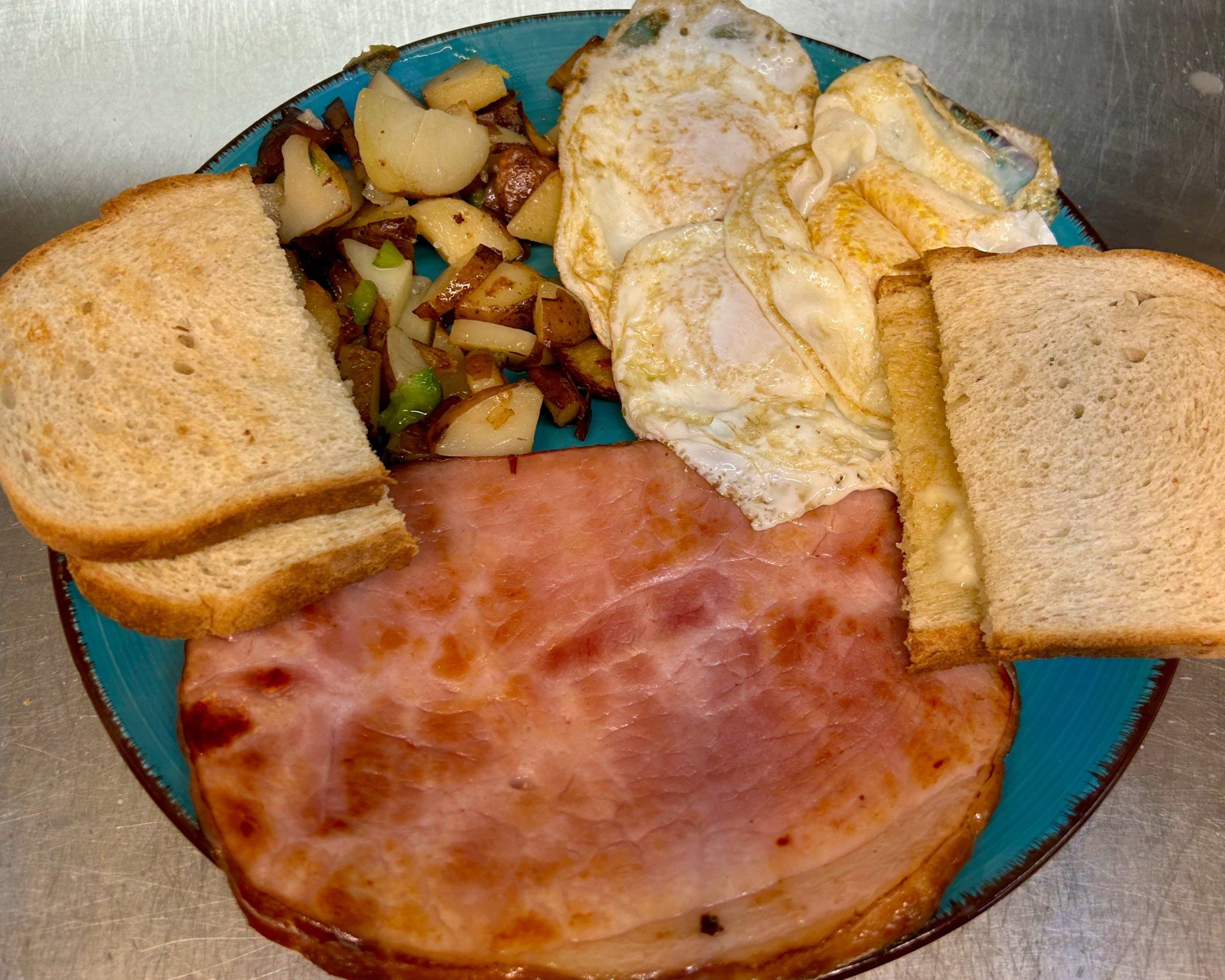 A blue plate topped with ham , eggs , potatoes and toast.