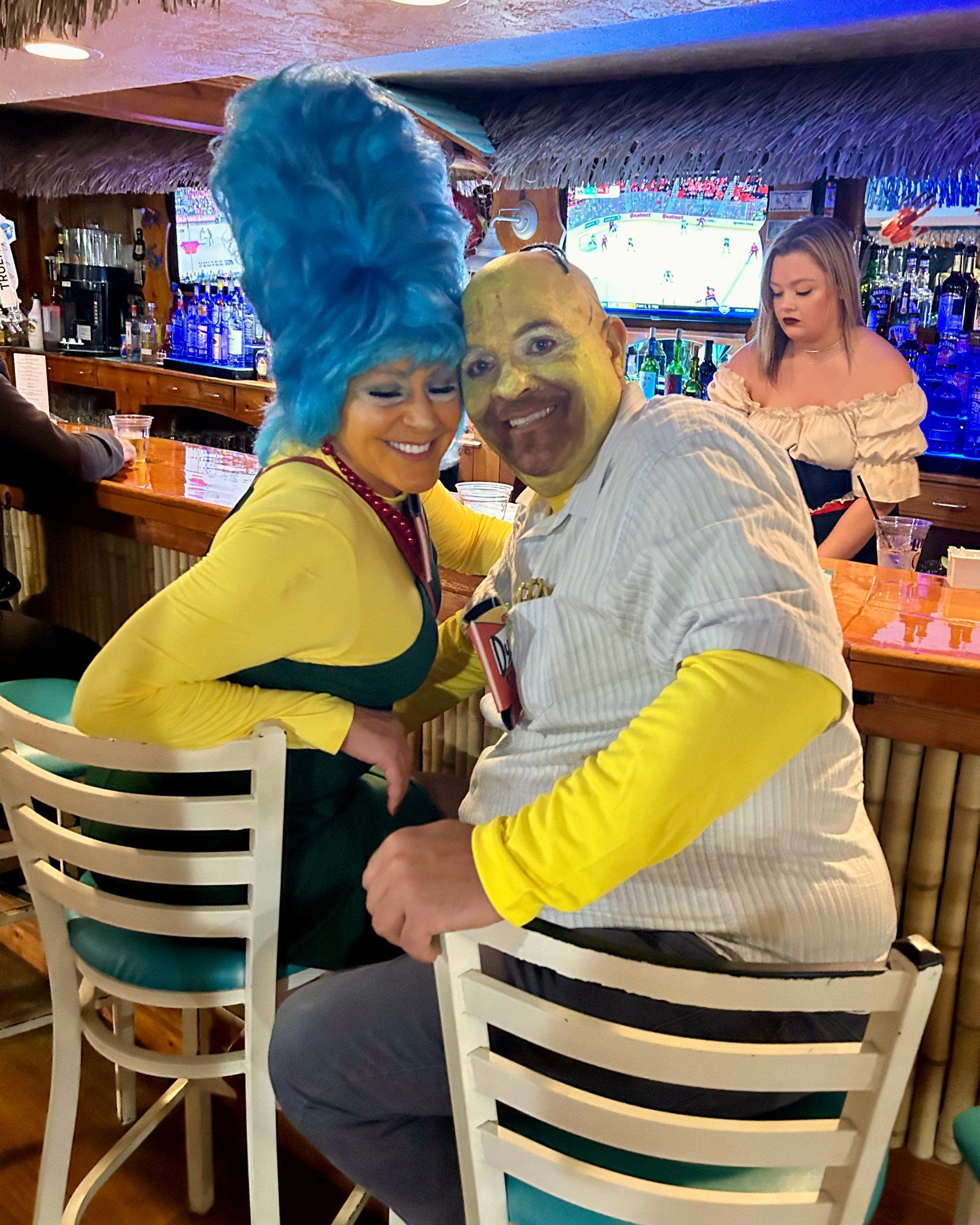 A man and a woman in shrek costumes are sitting at a bar.
