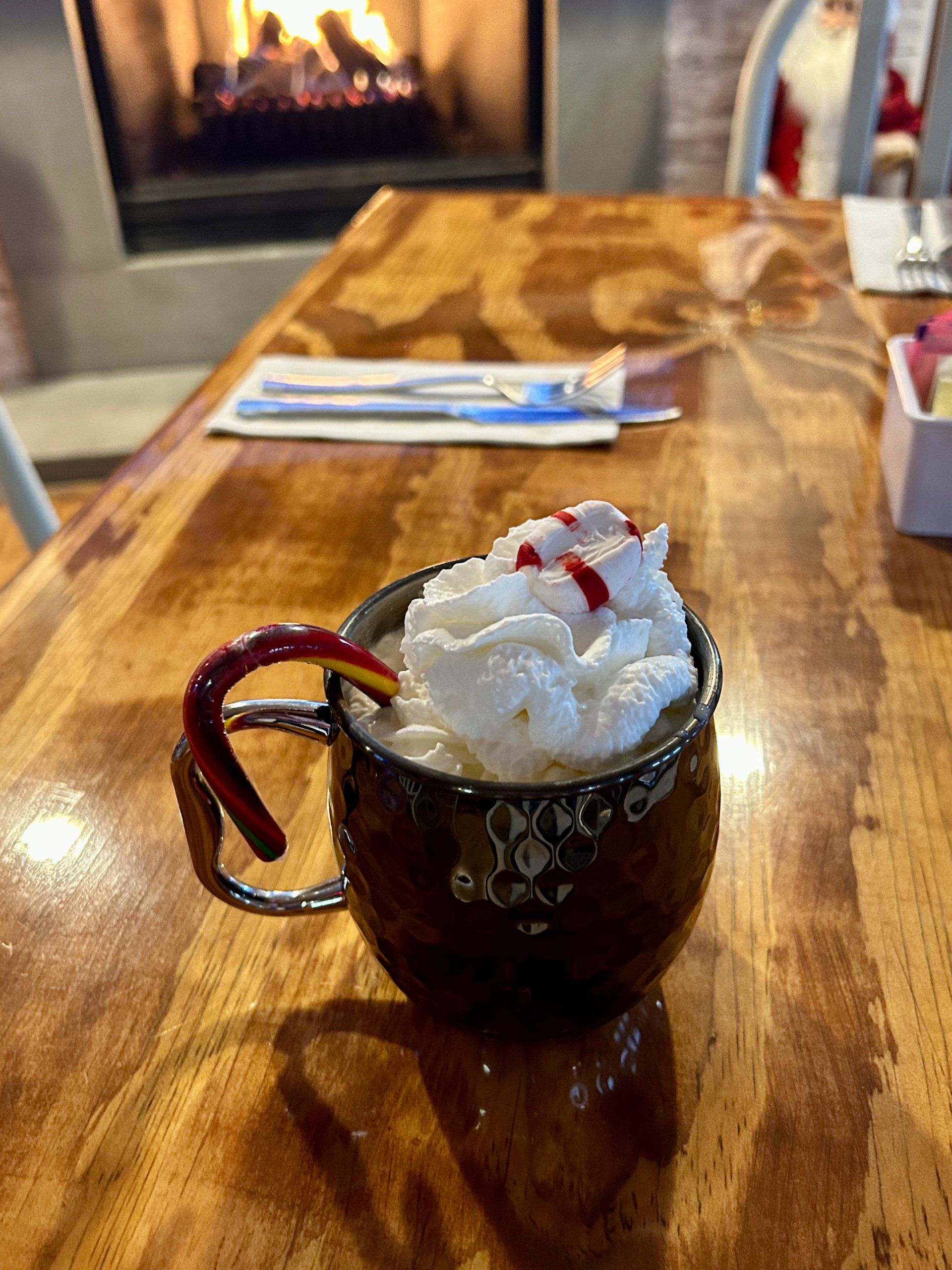 A cup of hot chocolate with whipped cream and candy canes on a wooden table.