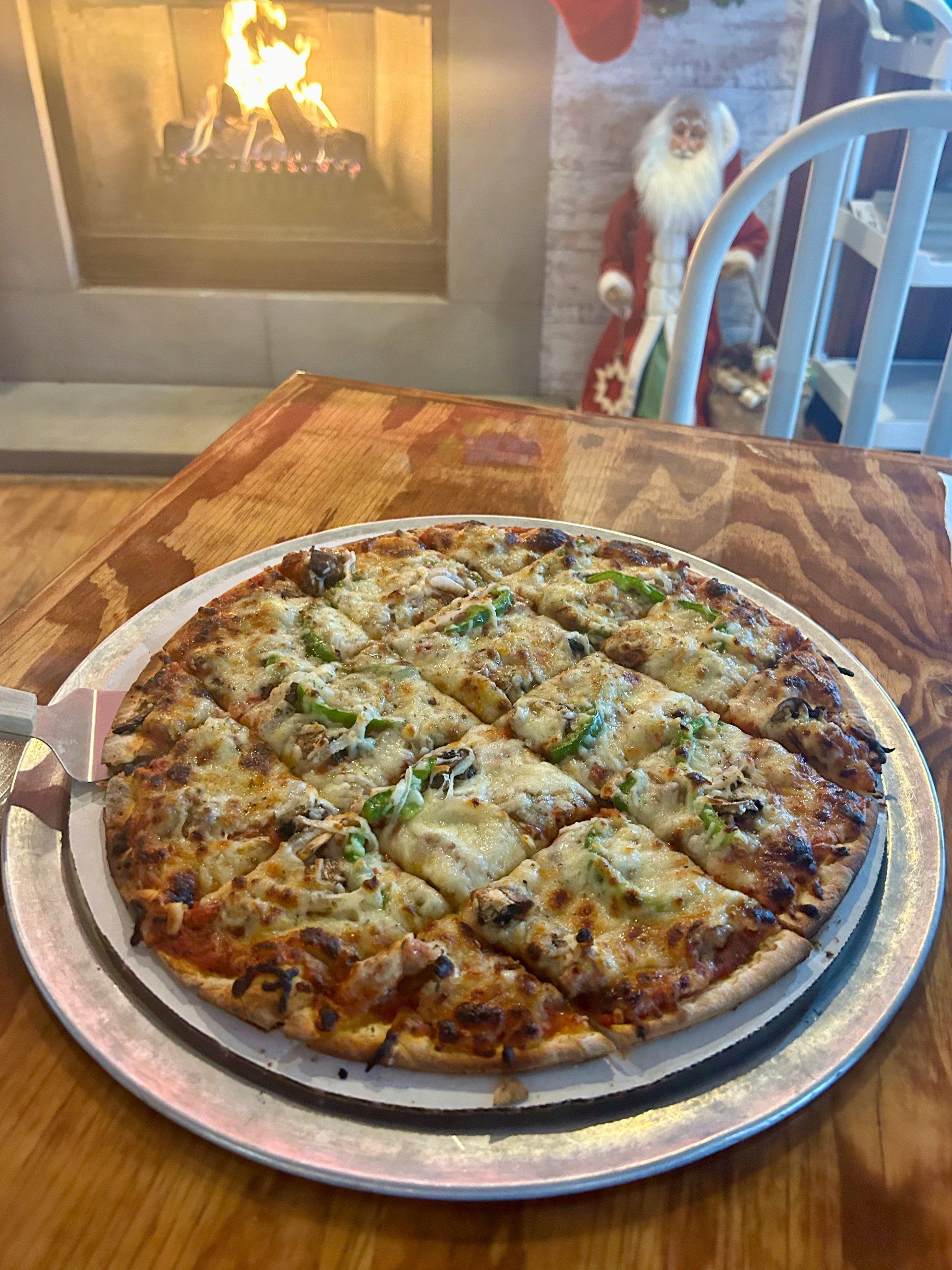 A pizza is sitting on a plate on a table in front of a fireplace.