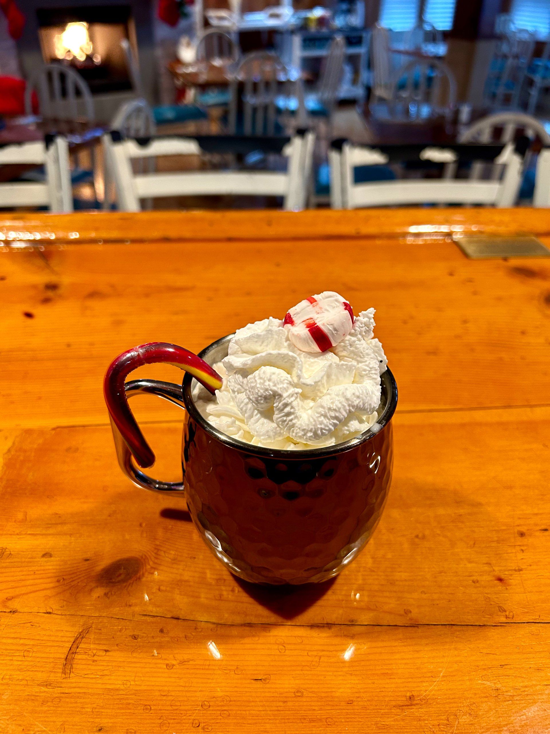 A cup of hot chocolate with whipped cream and candy canes on a wooden table.