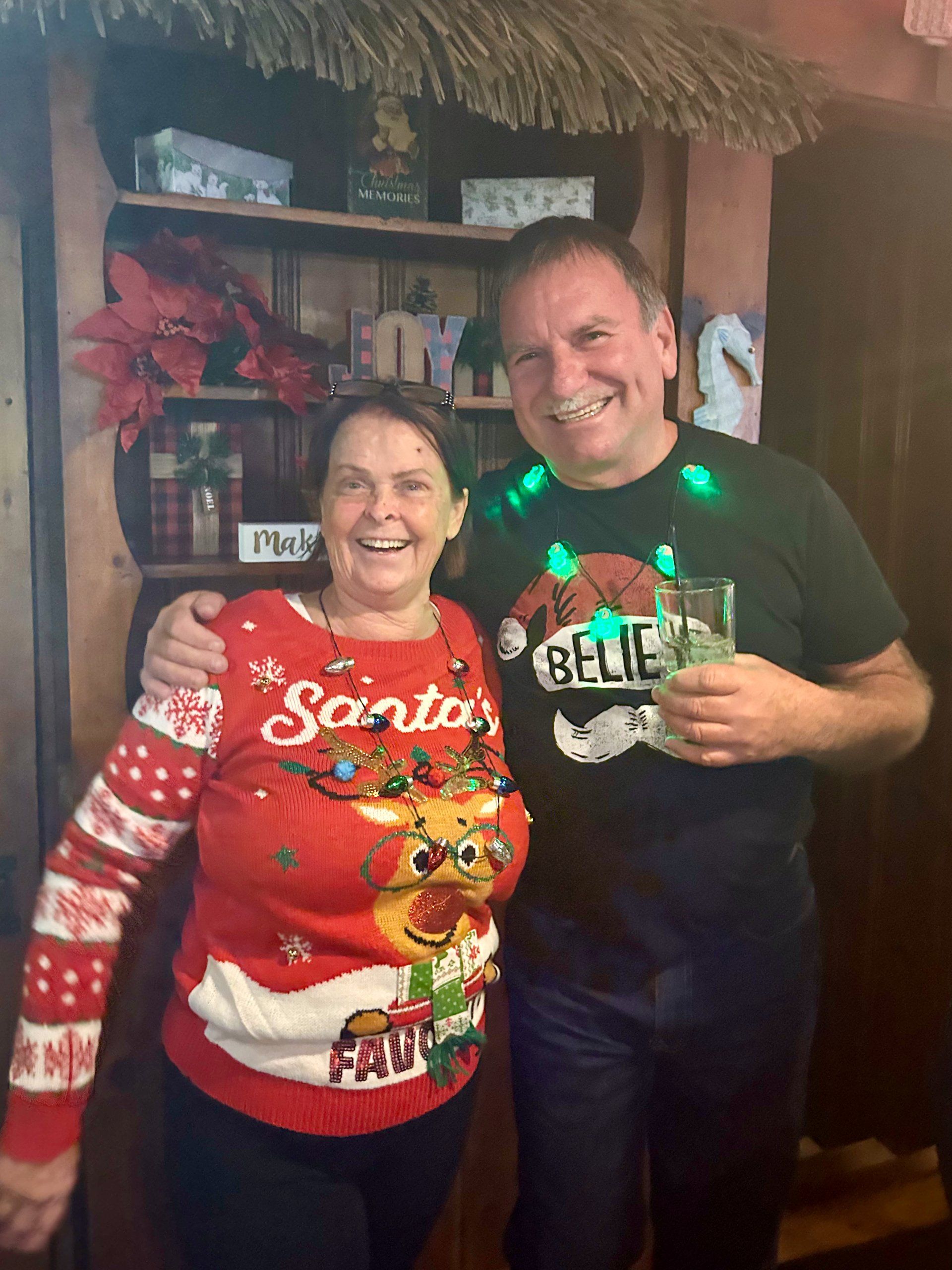 A man and a woman are posing for a picture . the woman is wearing a santa sweater.