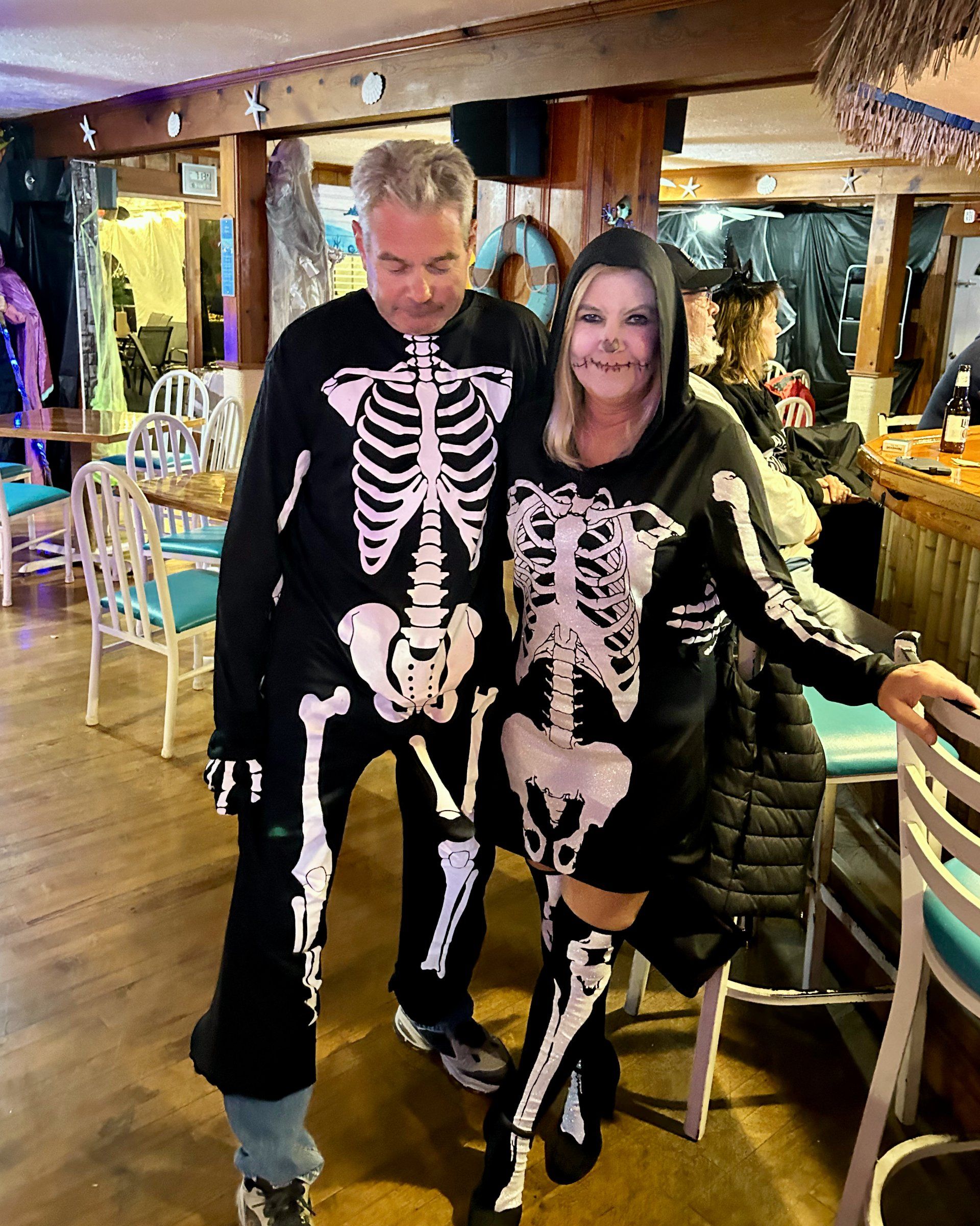 A man and a woman in skeleton costumes are posing for a picture in a restaurant.
