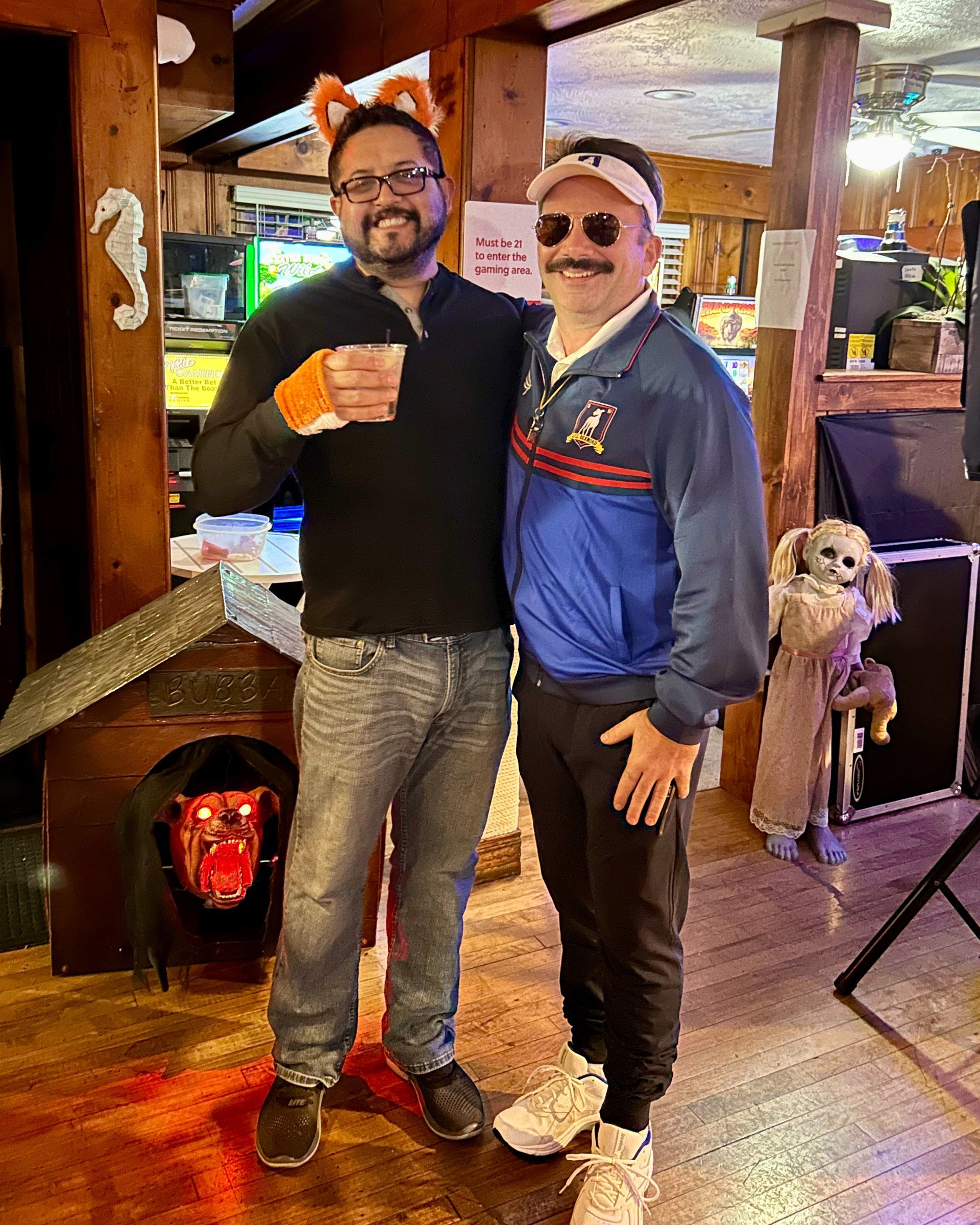 Two men are standing next to each other in a room and one of them is wearing a fox costume.