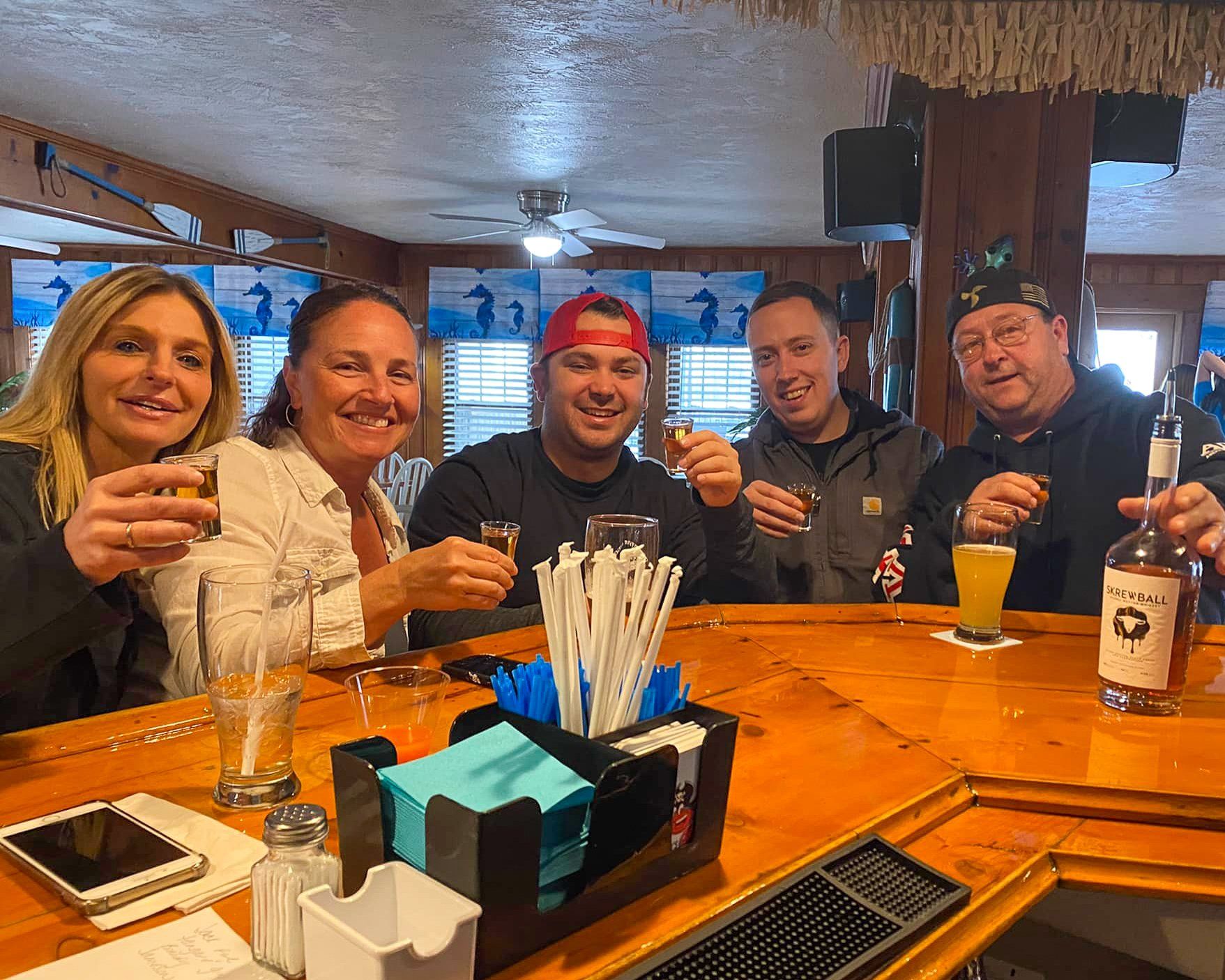 A group of people are sitting at a bar toasting with drinks.