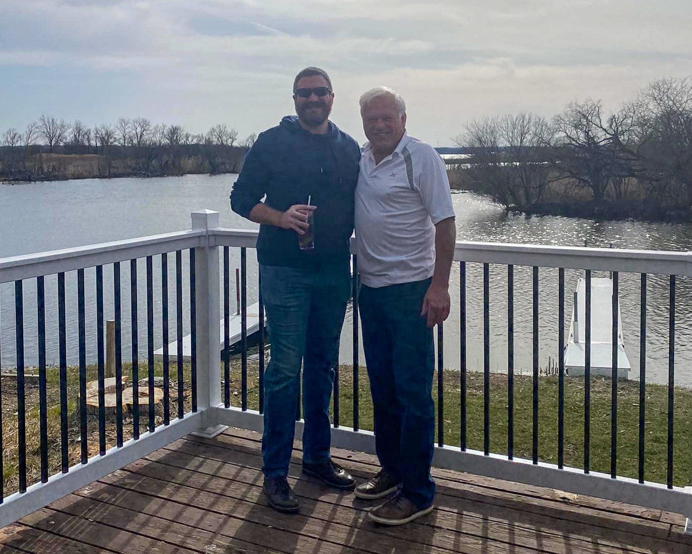 Two men are standing on a deck overlooking a lake.