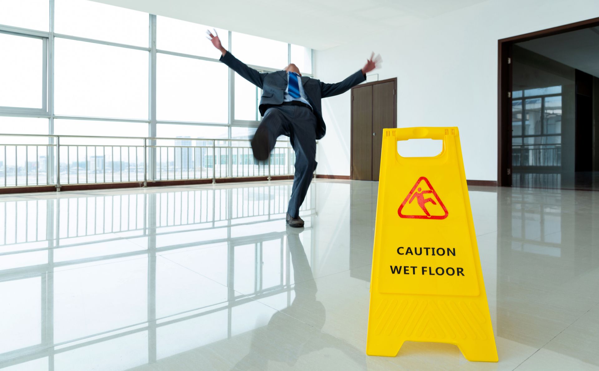 A man slips on a wet office floor near a yellow caution sign in a bright, modern building interior