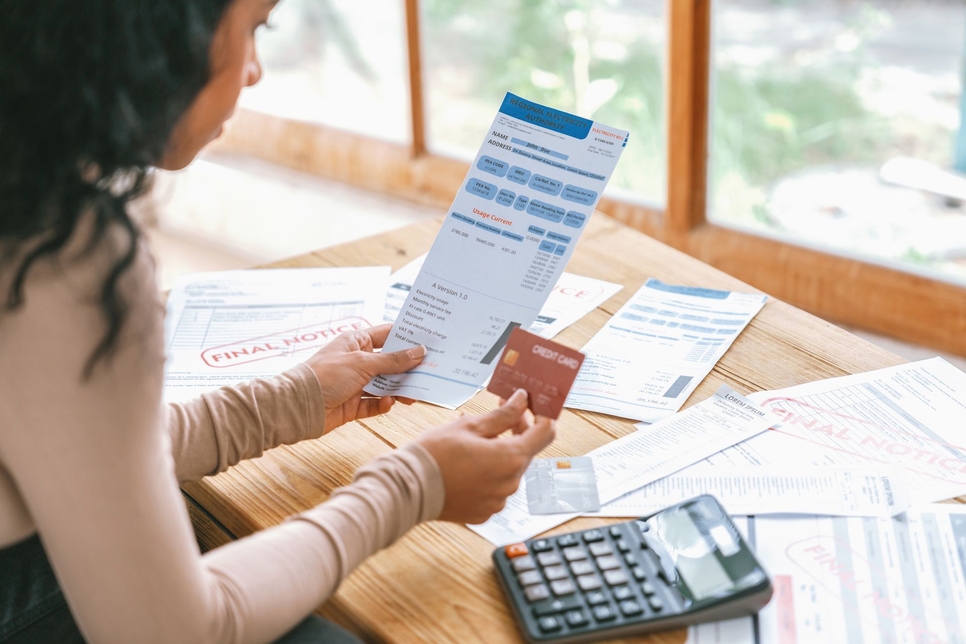 A woman is sitting at a table holding a credit card and a bill.