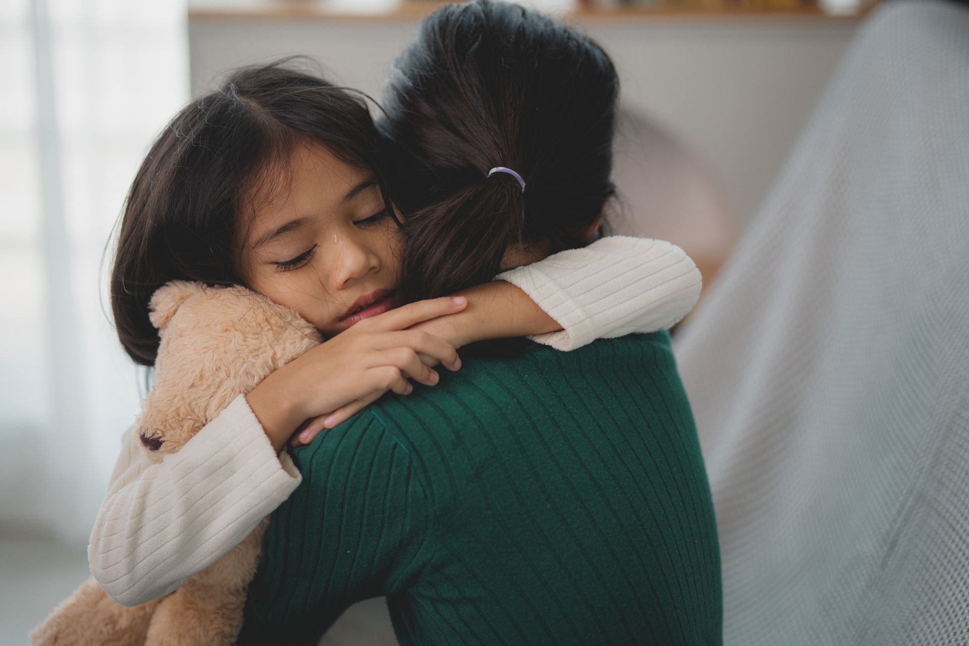 A little girl is hugging her mother while holding a teddy bear.