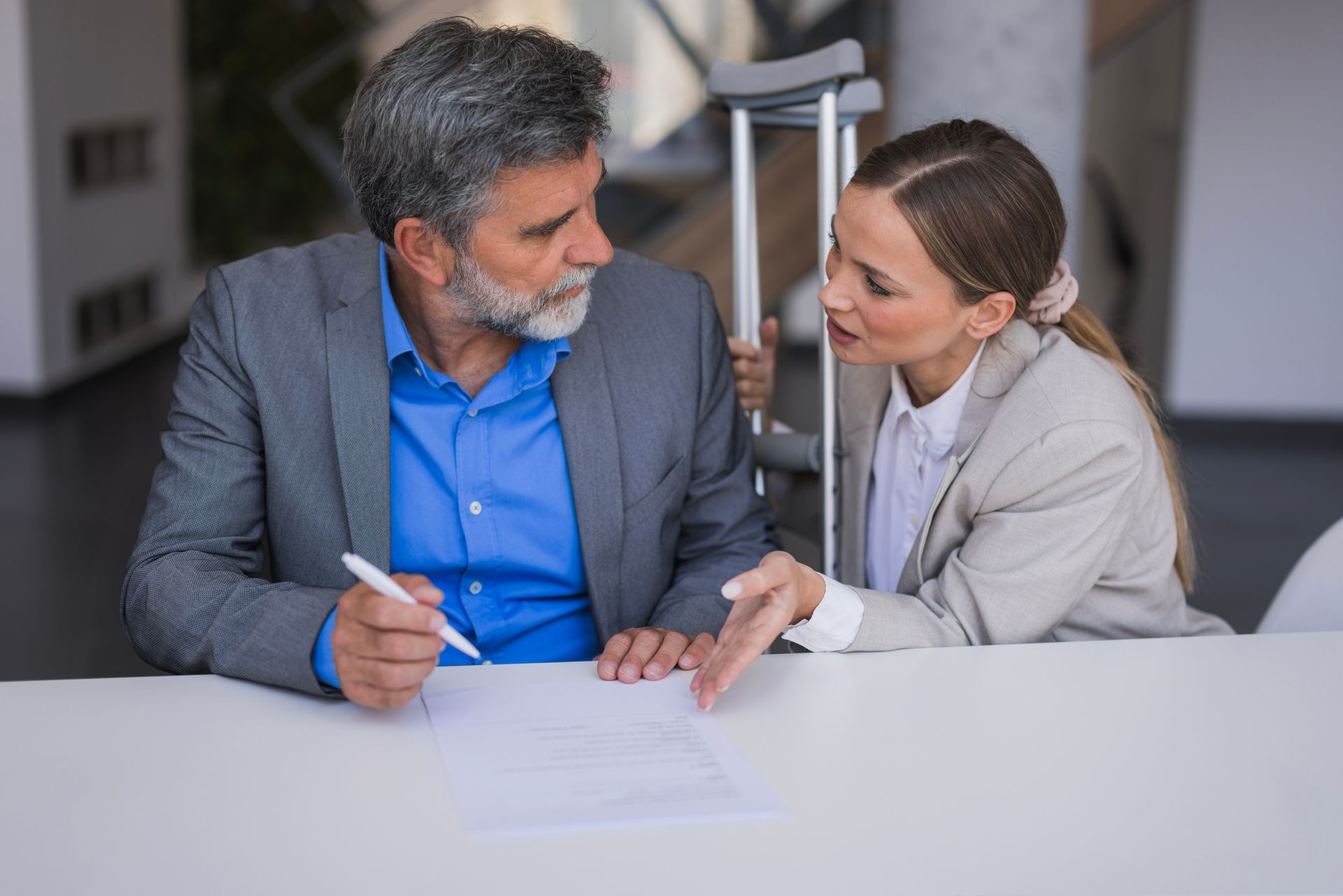 A man with crutches speaks with a female injury claim attorney inside an office.