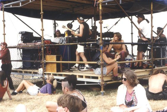 Festival stage with musicians and crew surrounded by a relaxed crowd