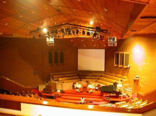Spacious church with red carpet, wooden walls, and a ceiling-mounted light rig.