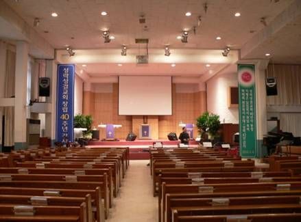 Church with wooden pews, stage lighting, and a large screen at the altar.