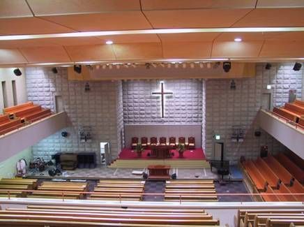 Bright sanctuary with glowing cross, red carpeted altar, and upper balconies.