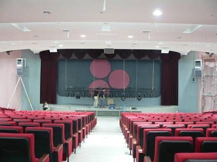 Modern auditorium with red seats and a dark stage with circular wall design.