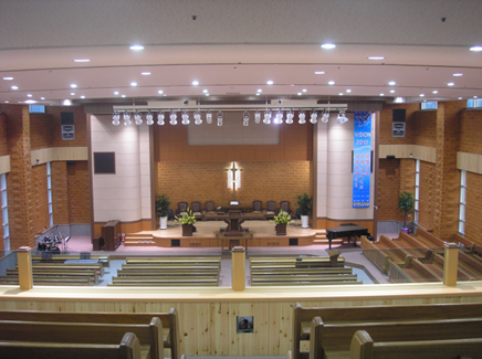 Large church with wooden pews, stage lighting, and a glowing cross centerpiece.