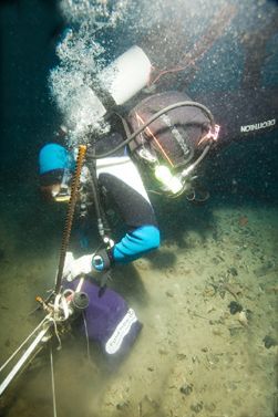 Diver in full scuba gear working underwater with tools and equipment.