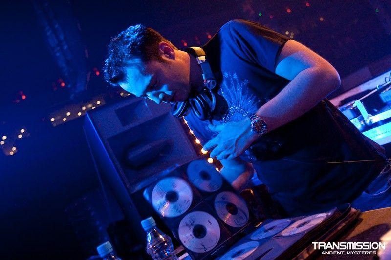 DJ performing with headphones, CDs, and a mixer at Transmission