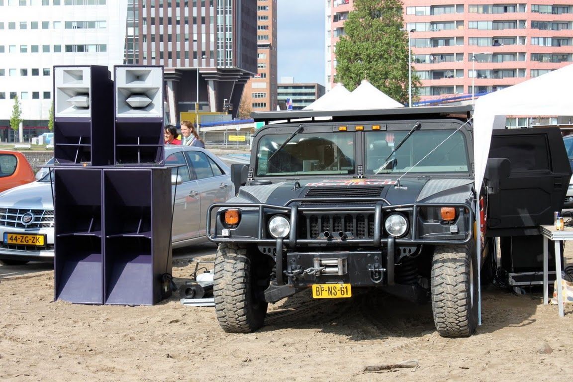 Black Hummer parked next to powerful Funktion-One speaker stack at outdoor event.