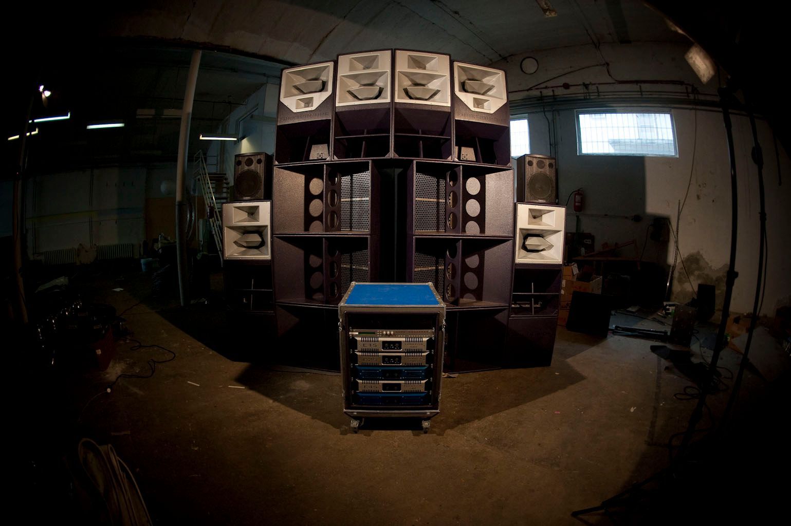 Huge indoor Funktion-One speaker stack with amp rack in a dimly lit warehouse.