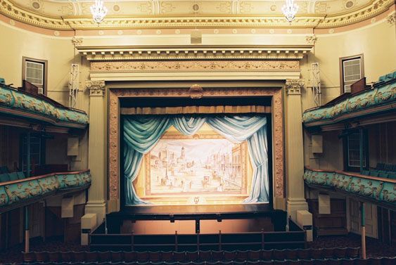 Historic theater stage with ornate decor and scenic painted curtain.