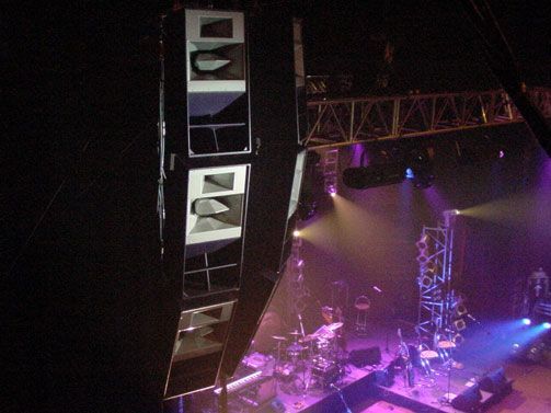 Suspended line array speaker system at a live music venue with stage lighting.