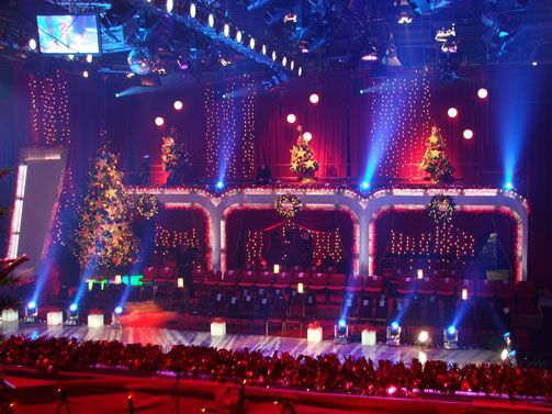 Colorful holiday-themed TV studio with lights, trees, and red seating.