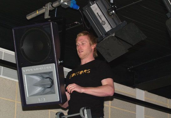 Man in black shirt installing a Funktion-One speaker on overhead rigging.